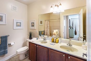 A bathroom with a toilet, sink, mirror, and pictures on the wall.
